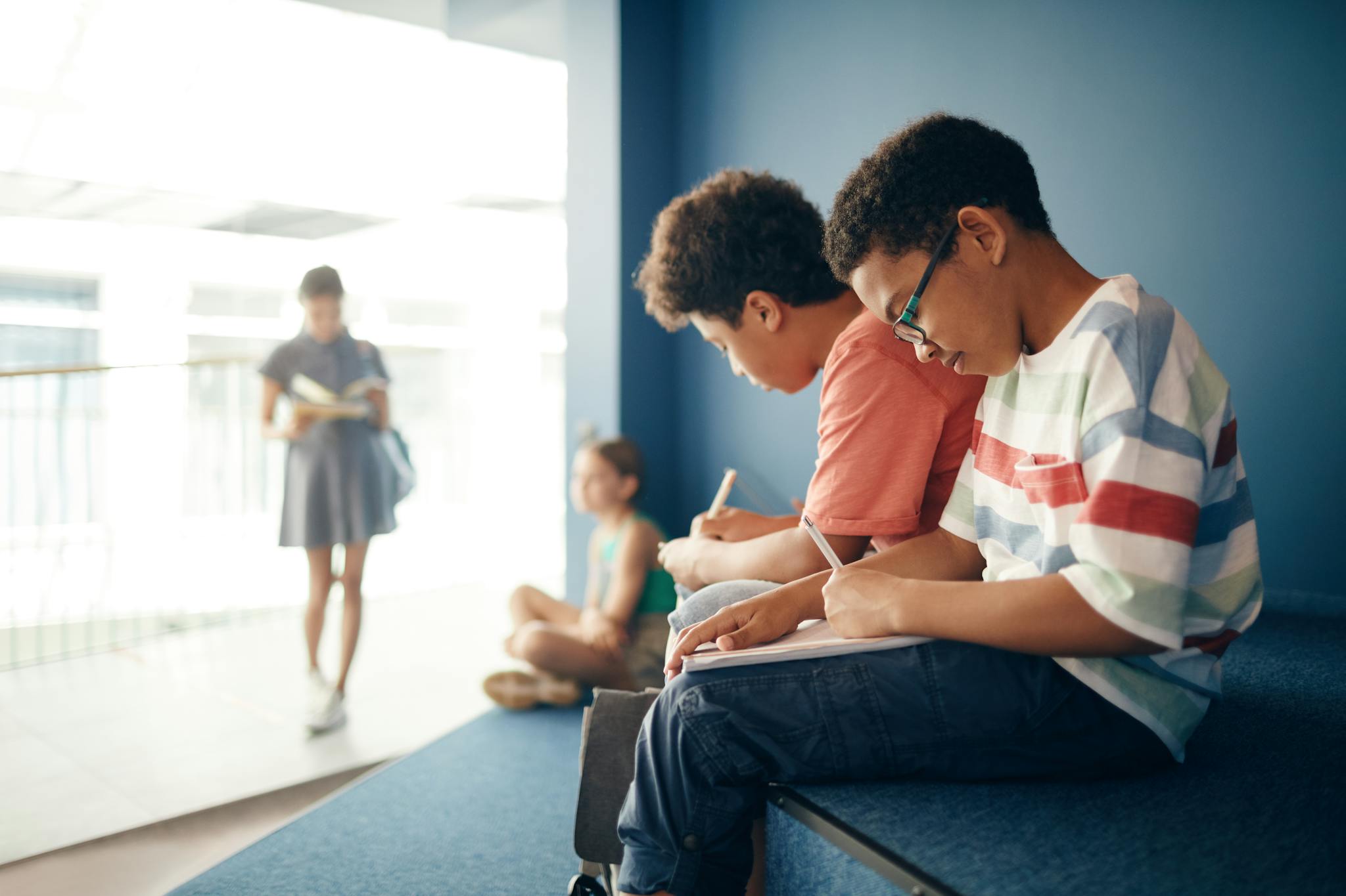 Diverse group of kids in a school hallway studying and writing notes.